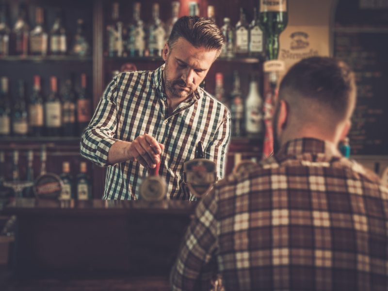 Handsome bartender pouring a pint of beer to customer in a pub.